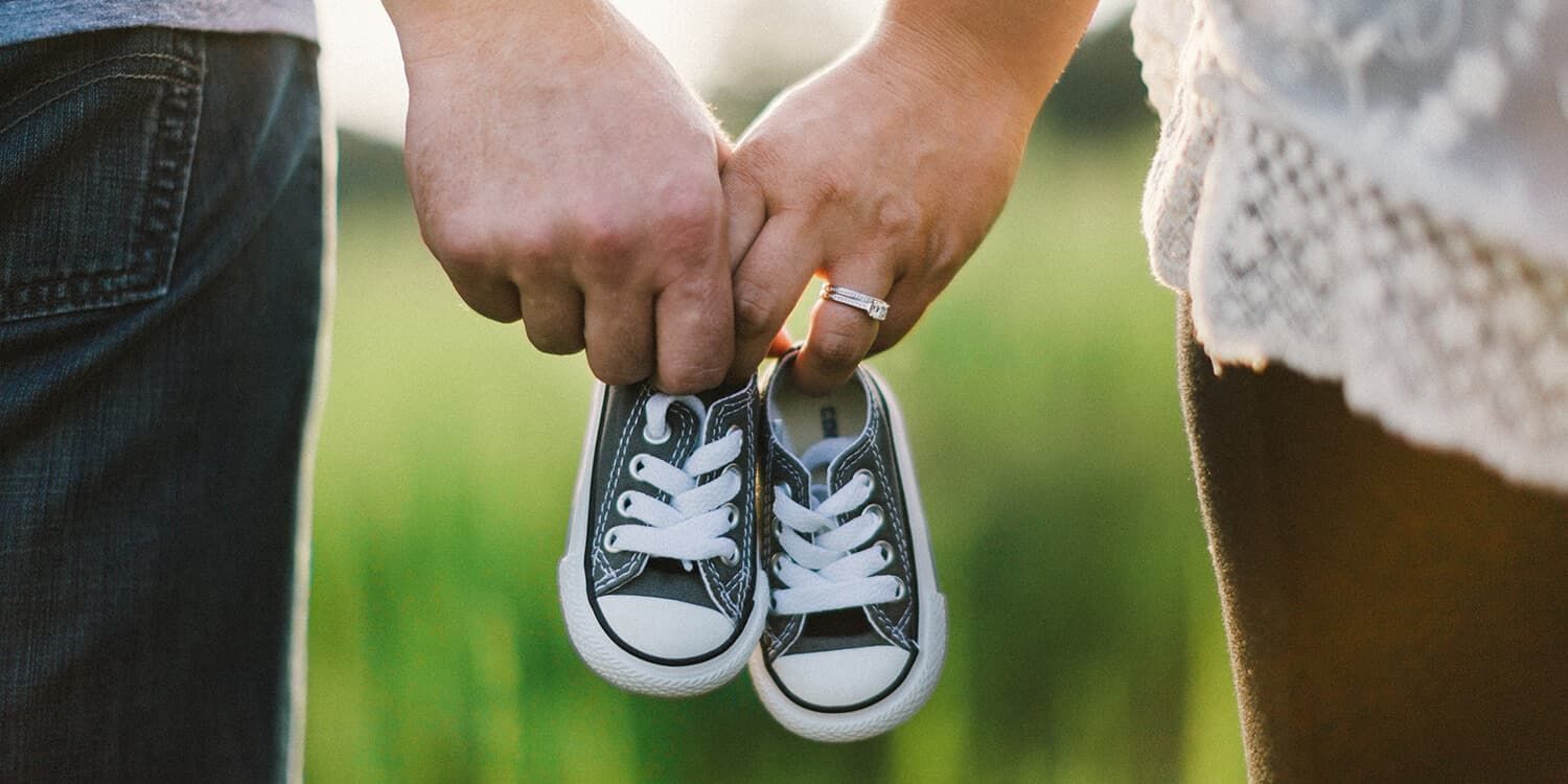 Schwangeres Paar hält gemeinsam Babyschuhe in den Händen.