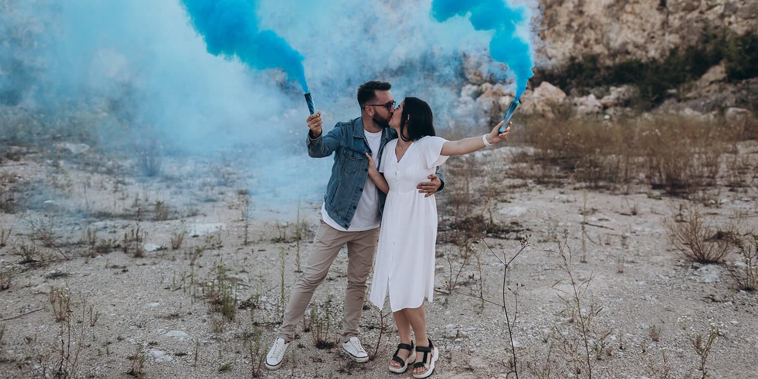 Zukünftige Eltern halten Party-Knaller mit blauer Farbe in die Höhe und zeigen so, dass ihr Baby ein Junge wird. 