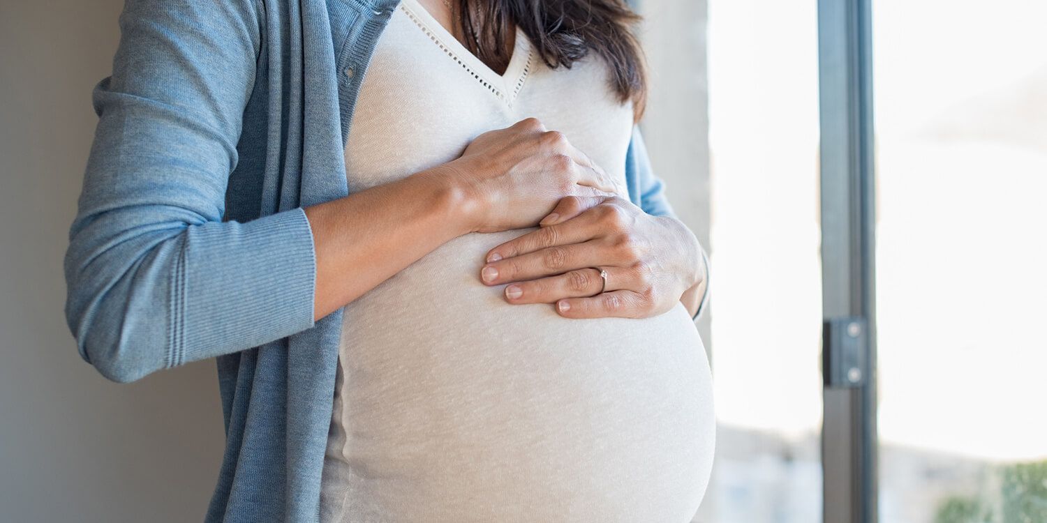 mulher grávida com as mãos na barriga olhando pela janela