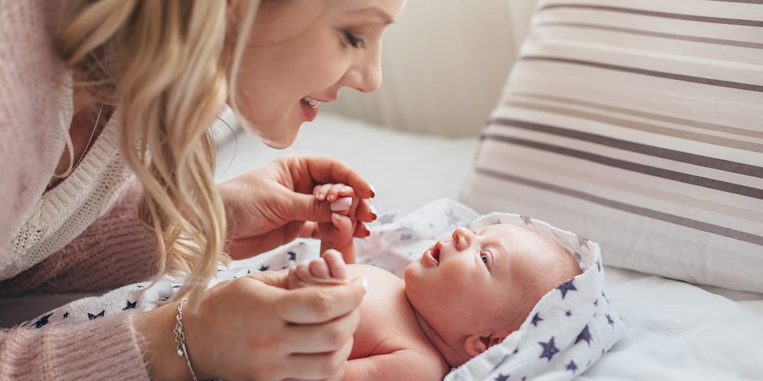 Mother bends over newborn baby and smiles at her