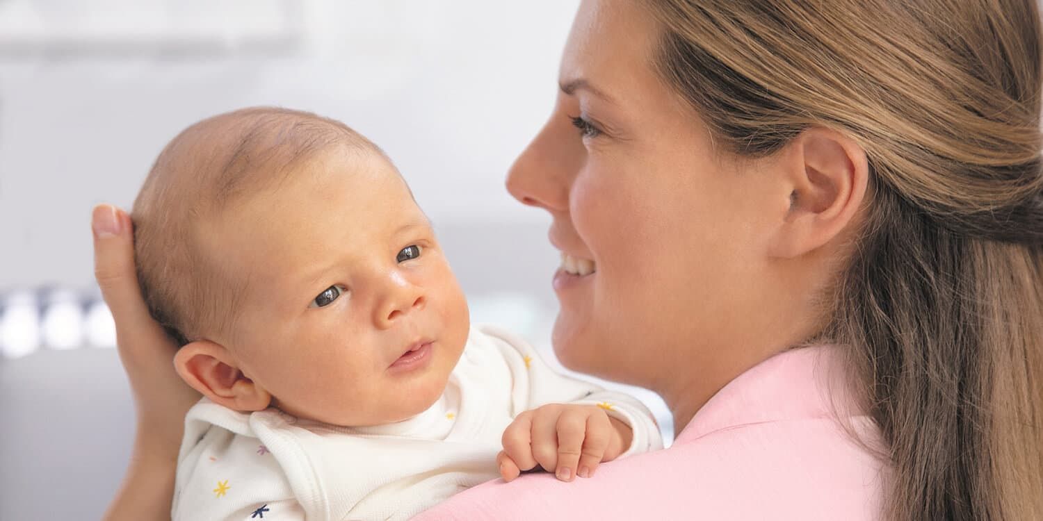 Mamma håller nyfödd på armen och ler