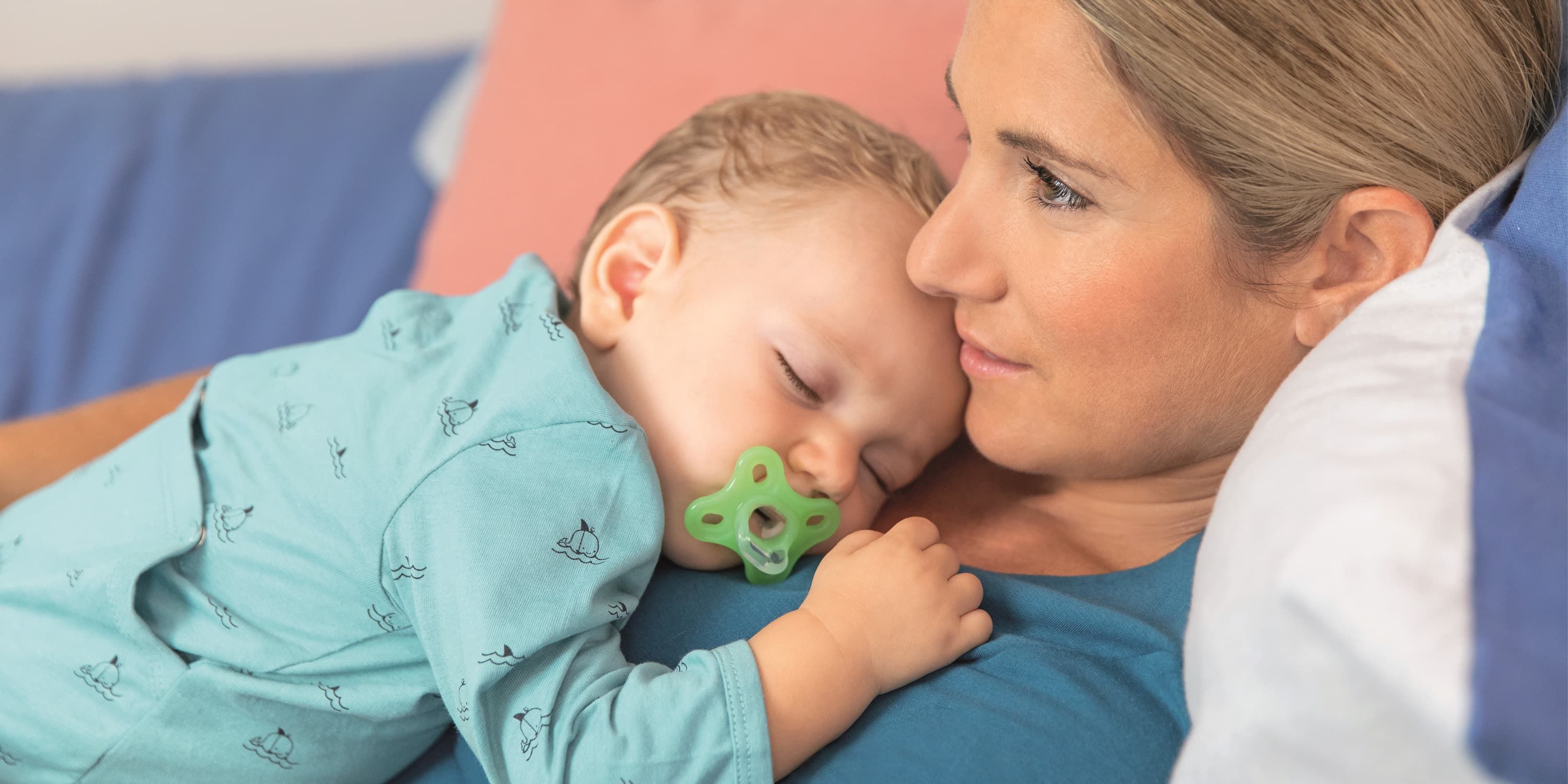 Junge Mutter kuschelt mit ihrem Baby, das an einem Schnuller saugt. 