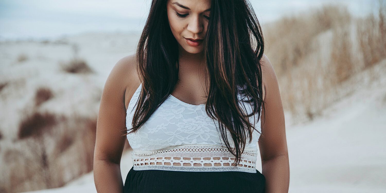 Pregnant woman stands on the beach and embraces her baby bump