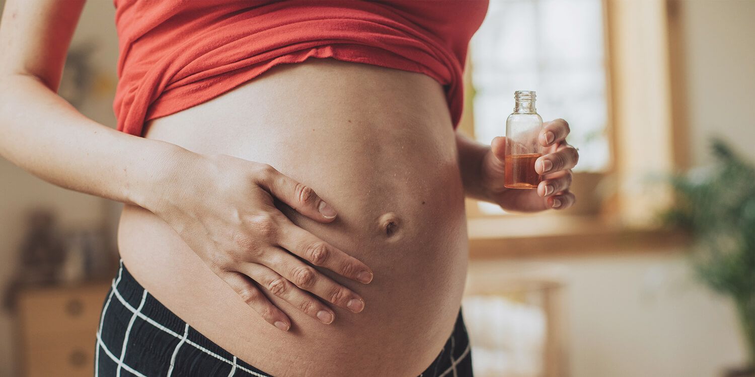 Pregnant woman rubs oil on her belly. 