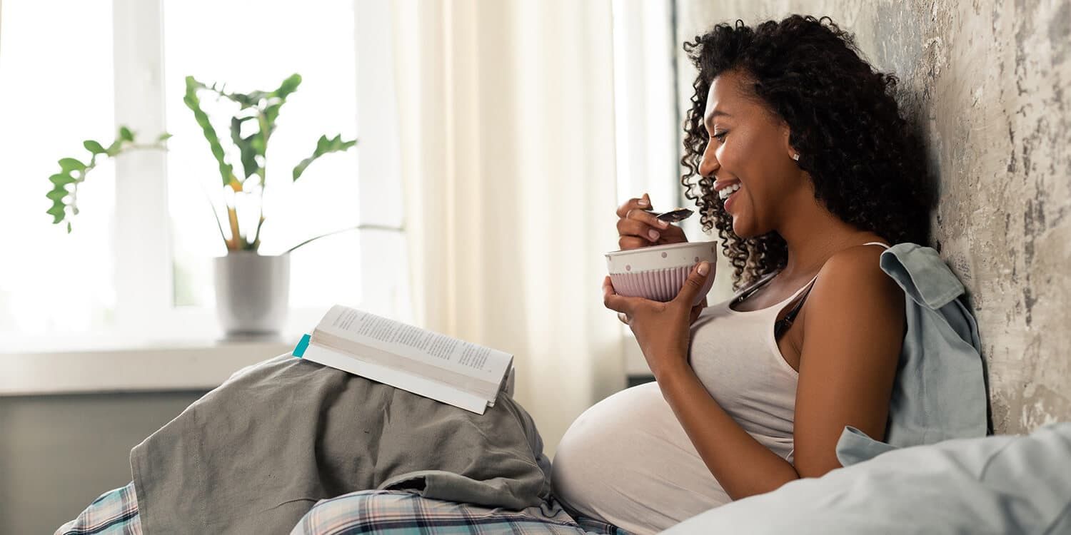 Una sorridente futura mamma fa colazione a letto.