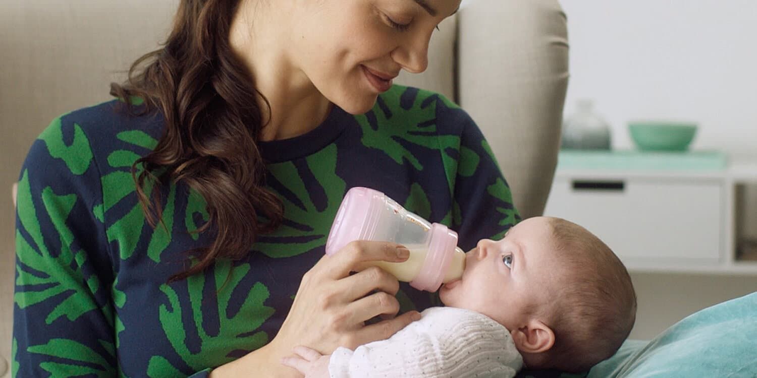 Mother sits on armchair and feeds baby with bottle