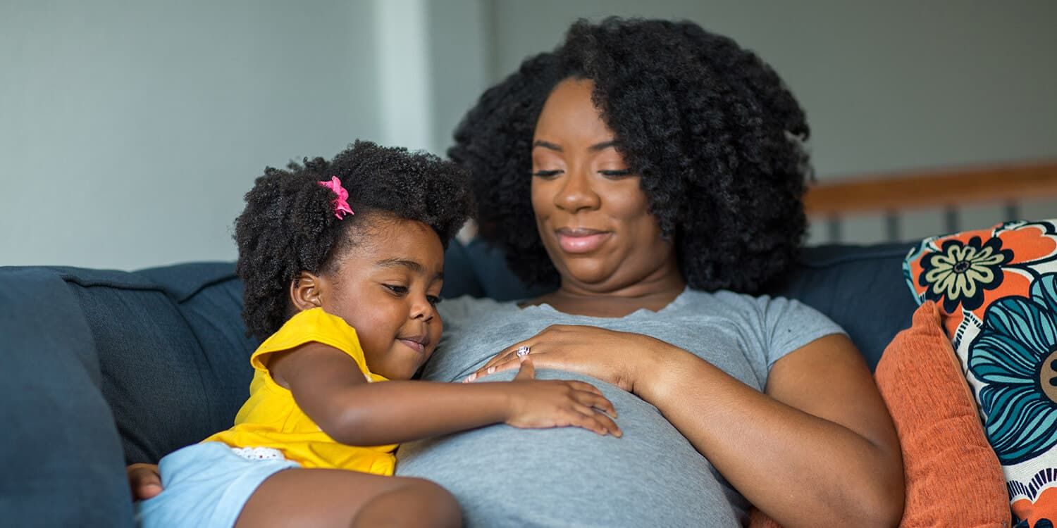 Une petite fille pose sa main sur le ventre de sa maman enceinte