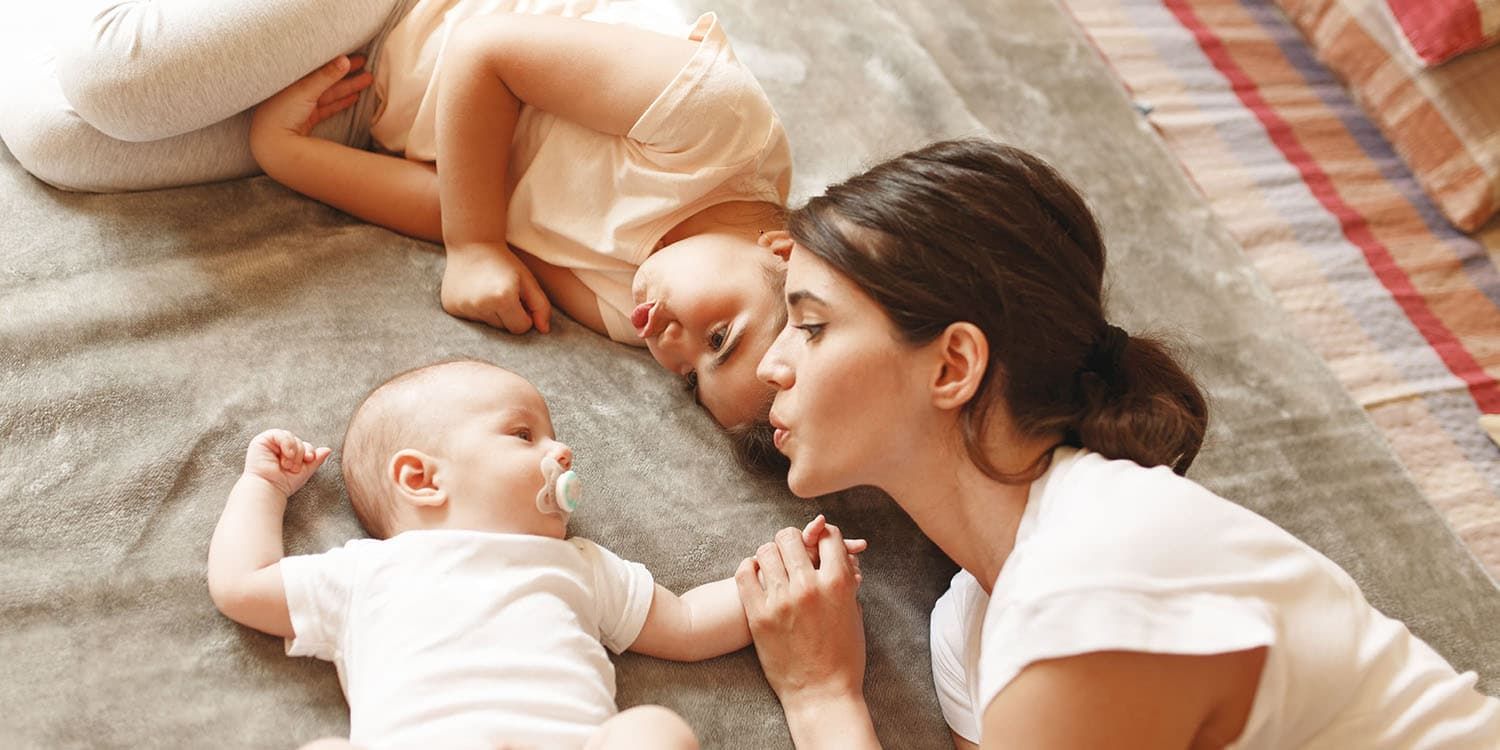 Mother and sibling cuddle with baby, baby has pacifier in mouth