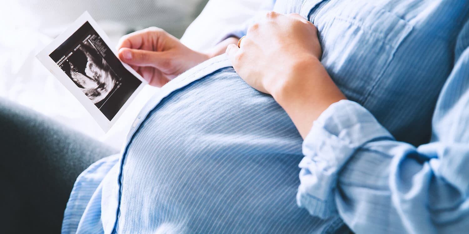 Pregnant woman holds an ultrasound image in her hand and has her other hand on her bump