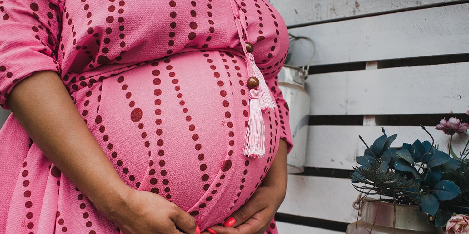 Image: Pregnant woman clasps her hands around her baby bump