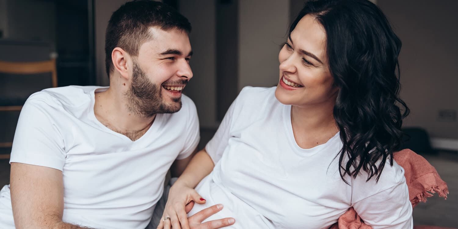 Una pareja joven embarazada en el sofá con las manos en el vientre de la mujer.