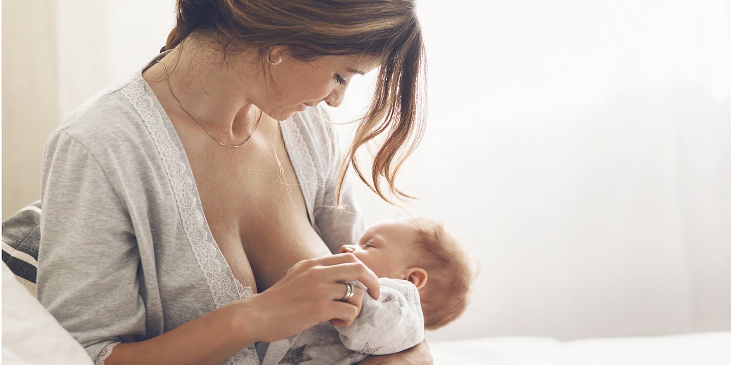 Junge Mutter stillt ihr Baby, hält es in ihren Armen und lächelt freudig