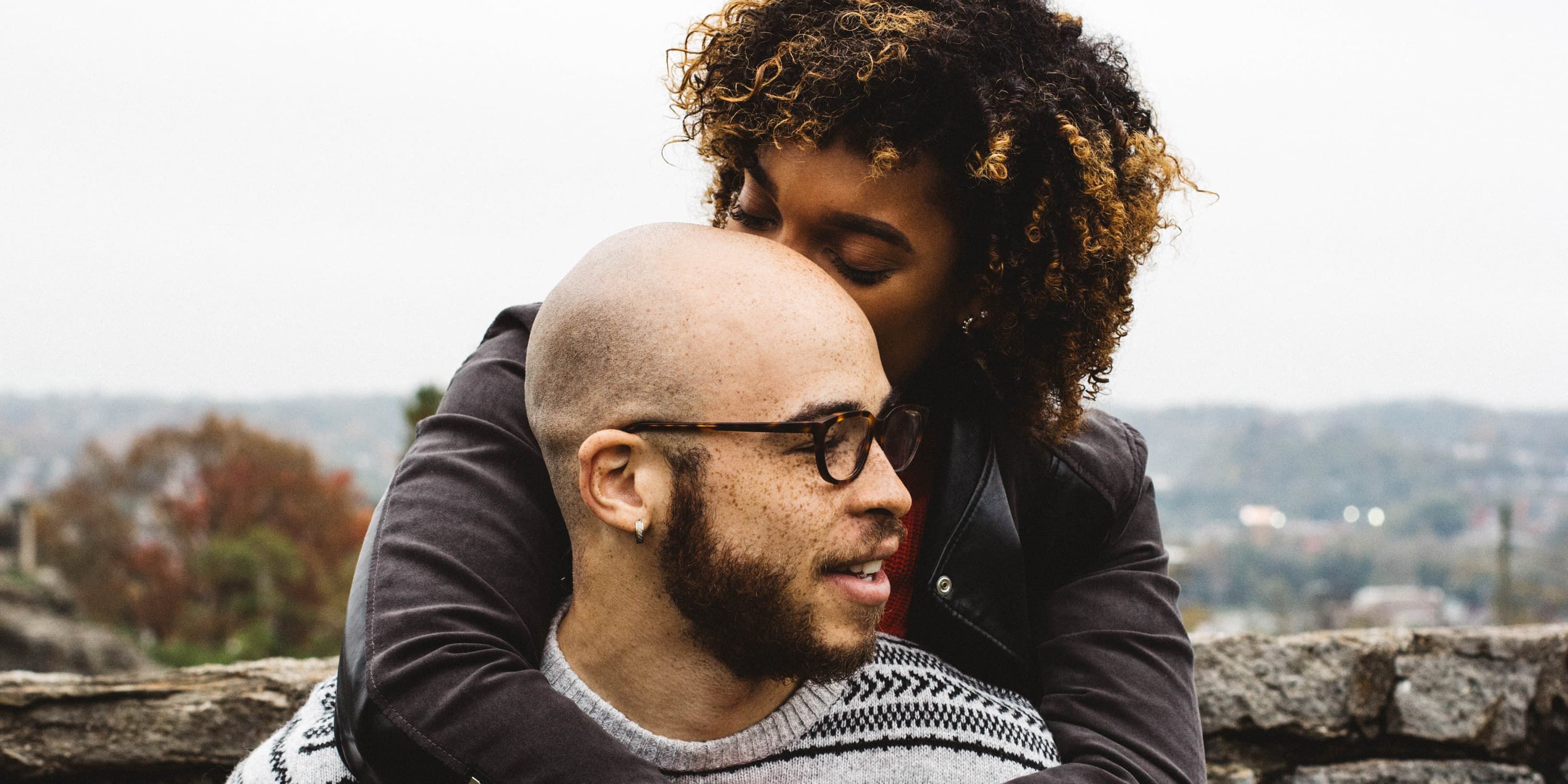 Woman hugs man from behind and kisses him on the head